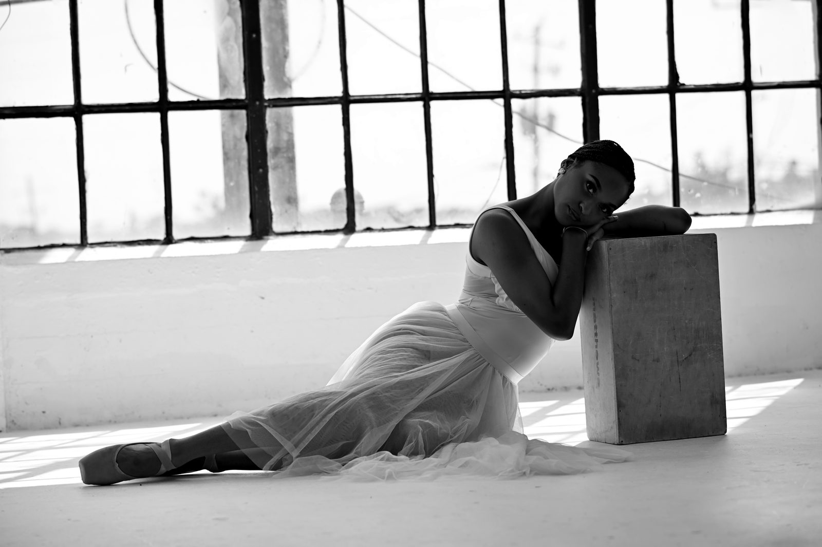 A. Joelle seated by a loft window, resting on a wooden cube