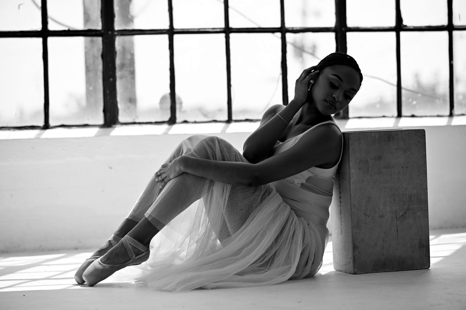 Seated on a cube with legs extended, pointe shoes forward