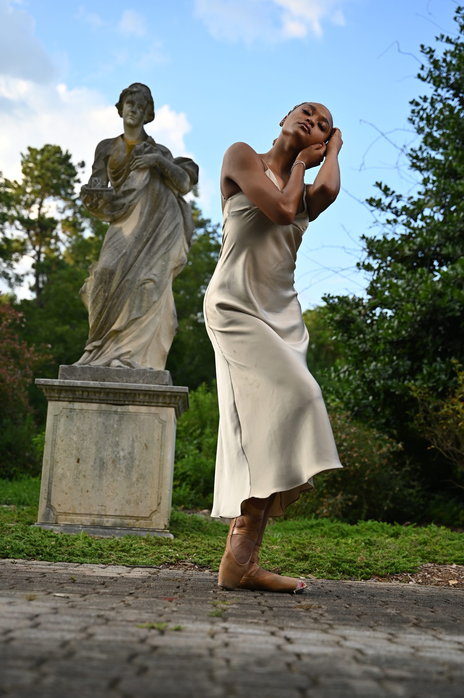 Hands in hair beside a park statue, satin dress